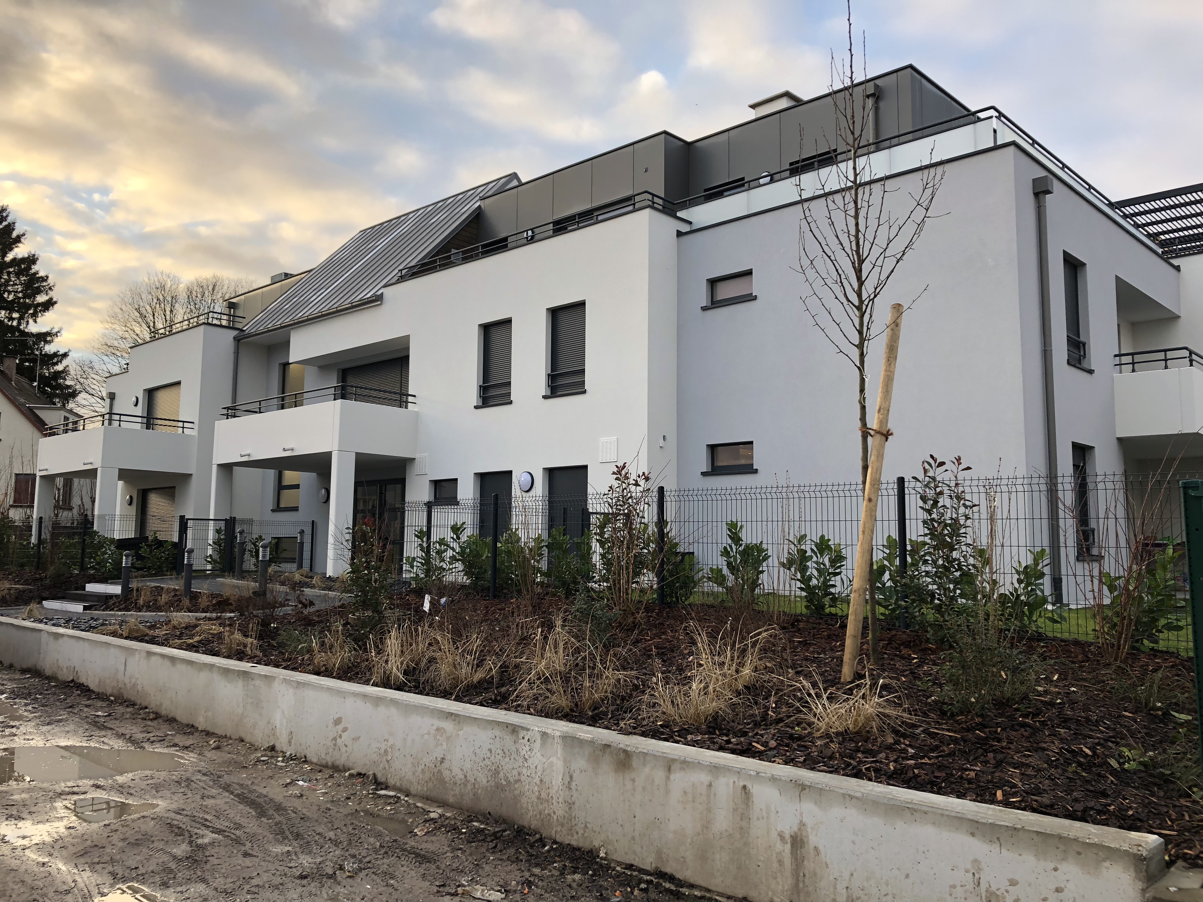 Vue d'un bâtiment moderne à plusieurs étages avec balcons, entouré de végétation et d'un espace aménagé.